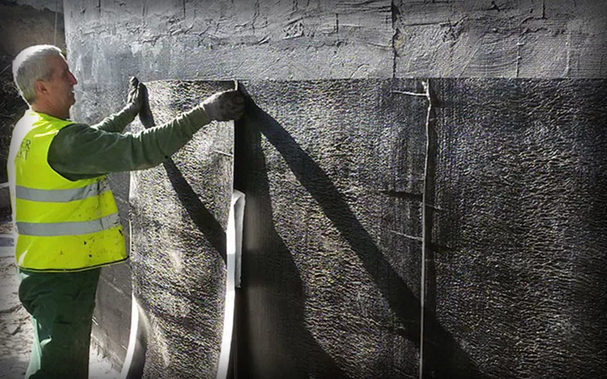 Pracownik kładzie hydroizolację na ścianę budynku